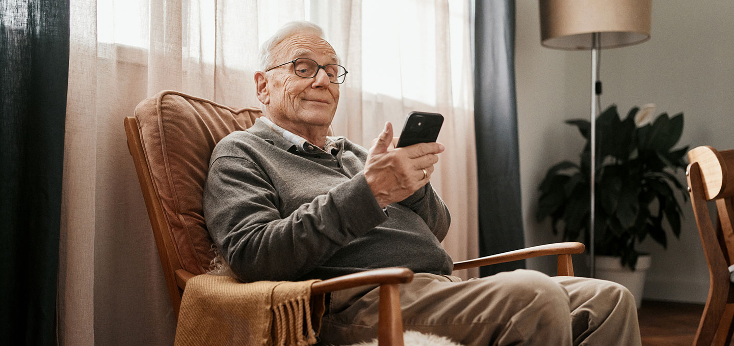 Ein älterer Mann sitzt in einem Sessel und schaut auf sein Smartphone