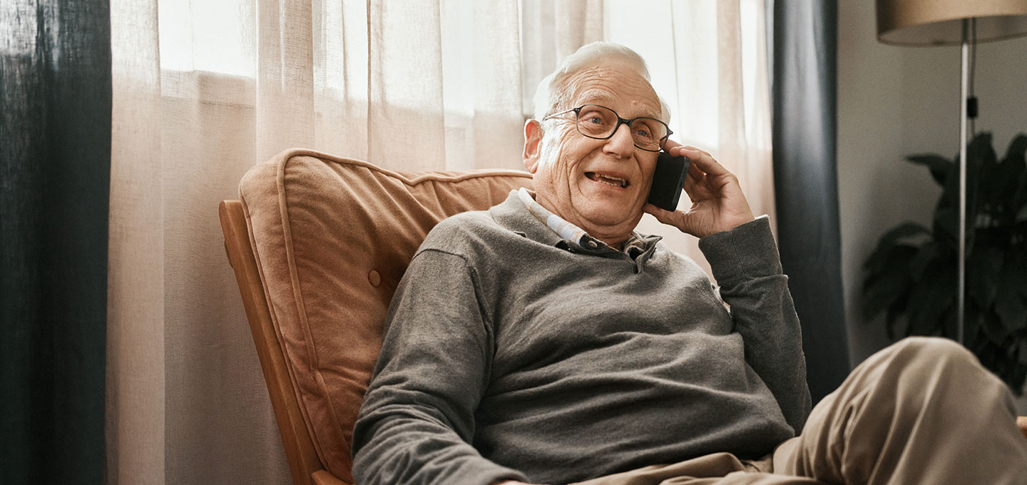 Älterer Mann sitzt mit Telefon auf Sessel