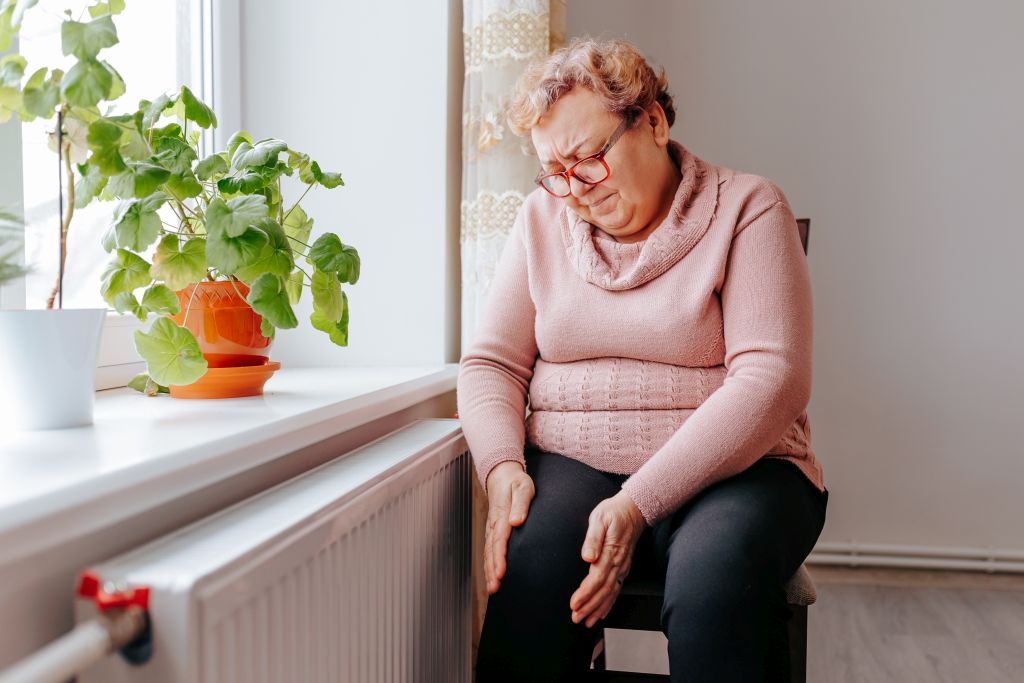 Abnehmen im Alter: Eine ältere Dame schaut mit schmerzverzerrtem Gesicht auf ihr Knie