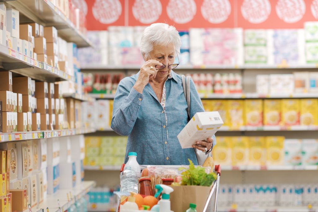 Alterssichtigkeit: Eine ältere Dame hat beim Einkaufen Schwierigkeiten beim Erkennen des Produkts in ihrer Hand