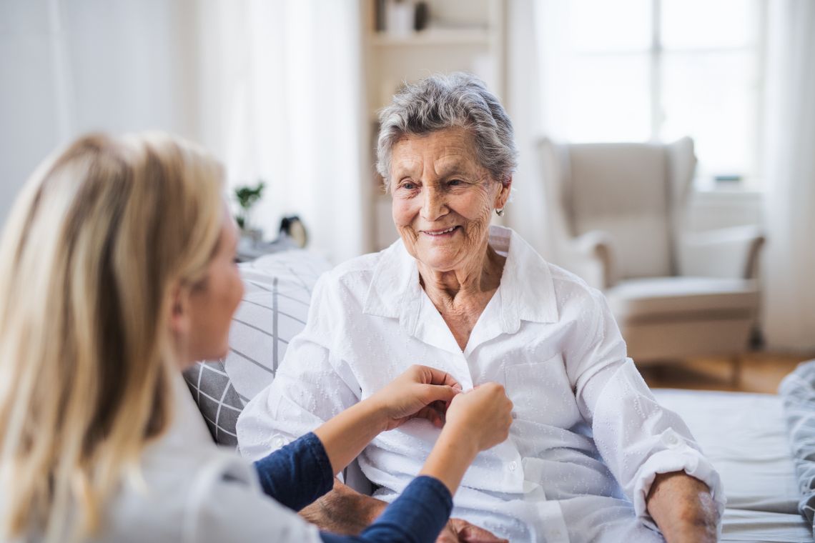 Eine Pflegerin hilft einer Seniorin beim Anziehen