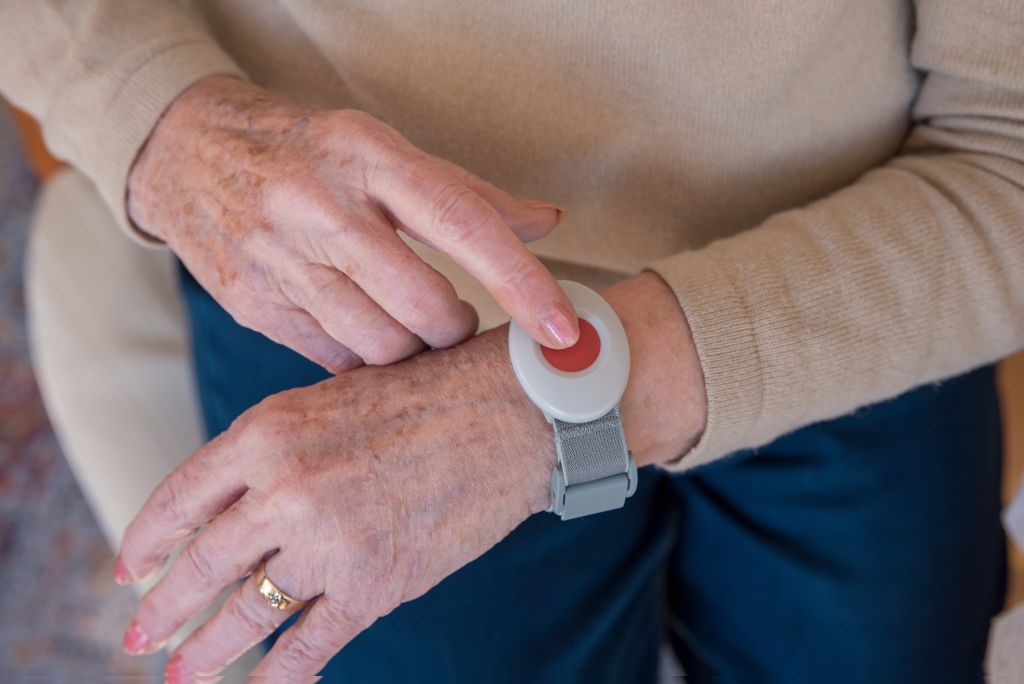 Erste Hilfe für Senioren: Eine ältere Dame drückt auf einen Hausnotruf-Knopf, der sich an ihrem Handgelenk befindet