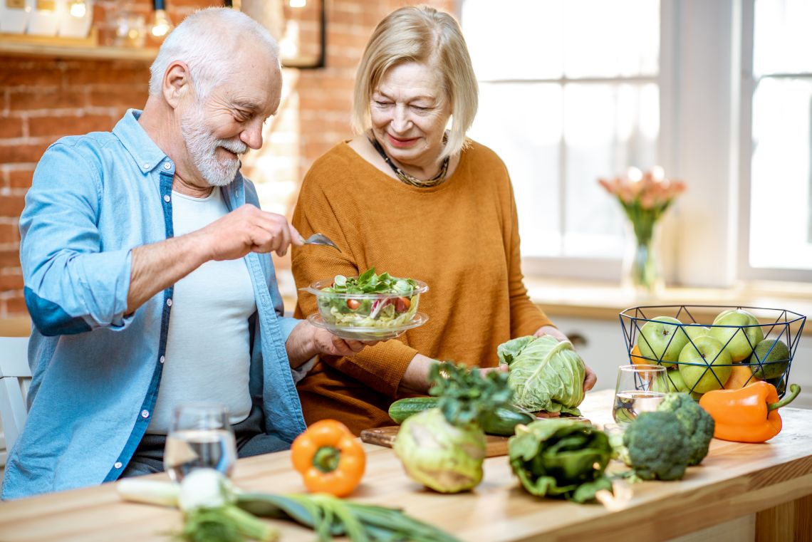 Älteres Ehepaar isst gemeinsam einen Salat mit gesunden Lebensmitteln zur besseren Blasengesundheit