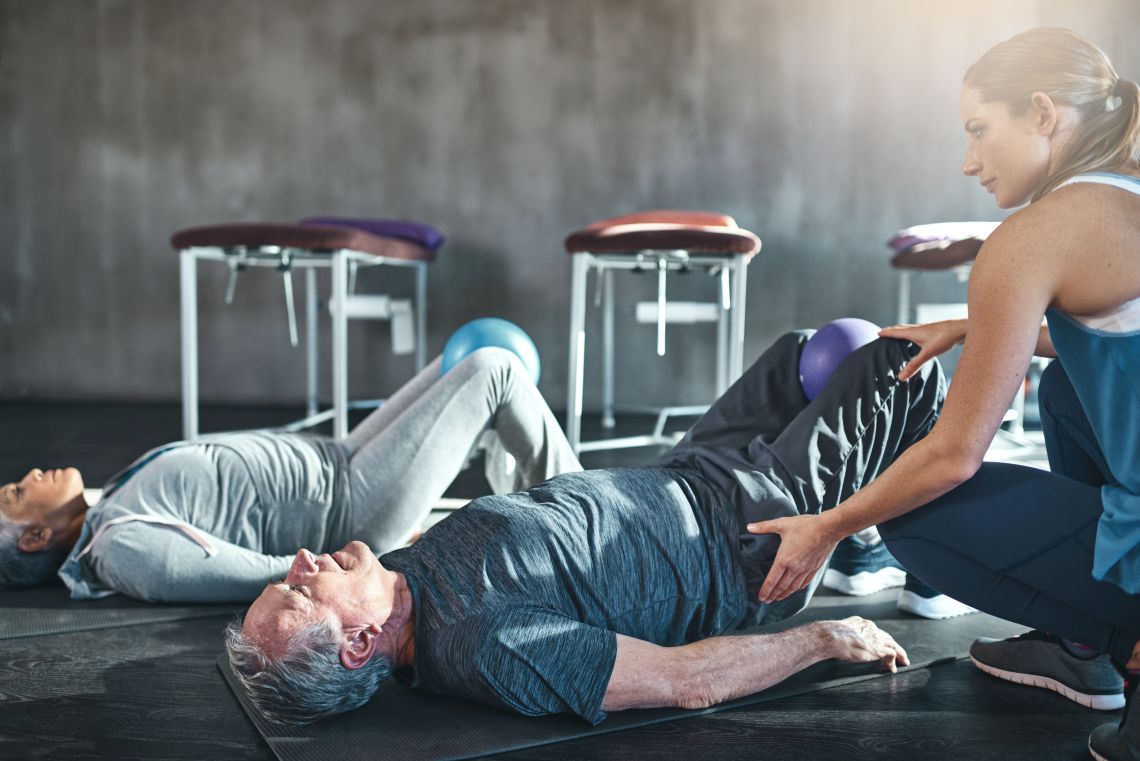 Eine Physiotherapeutin zeigt Übungen mit dem Medizinball für eine gesunde Blase bei Mann und Frau.