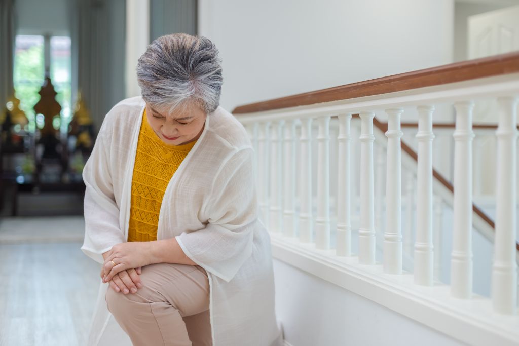 Eine ältere Dame fasst sich nach dem Treppensteigen vor Schmerzen ans Knie