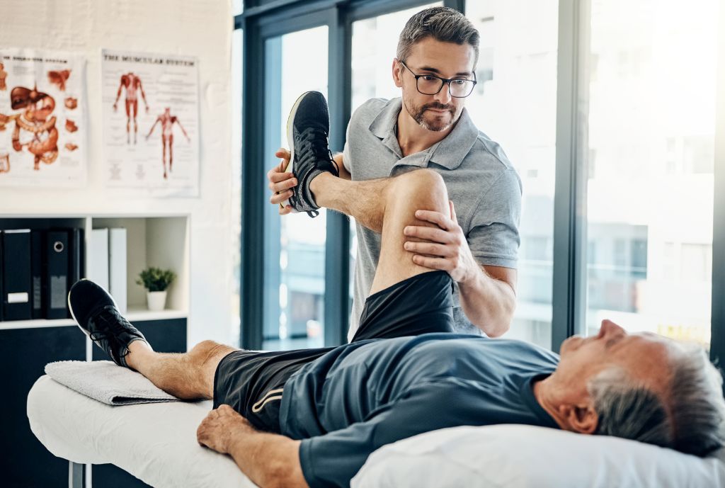Kraftlose Beine beim Treppensteigen: Ein Physiotherapeut führt mit einem älteren Mann Übungen zur Stärkung der Beinmuskulatur durch