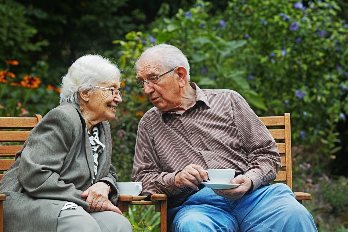 Ein älteres Ehepaar sitzt gemeinsam kaffeetrinkend im Garten