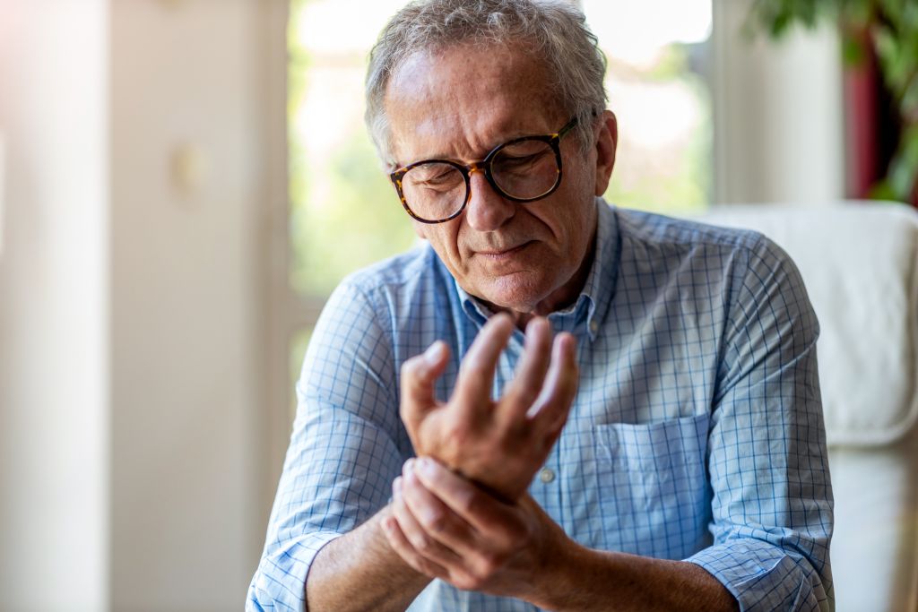 Osteoporose im Alter: Ein älterer Herr tastet sein Handgelenk ab und verzieht dabei das Gesicht vor Schmerzen